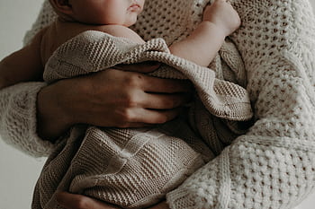 A tender moment of a mother holding her baby wrapped in a blanket, exuding warmth and care. HD wallpaper
