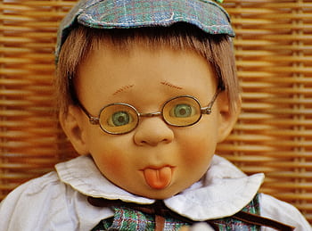 Adorable child-like doll wearing glasses and hat, playfully sticking out its tongue in a humorous portrait. HD wallpaper