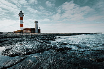 A beautiful lighthouse on a rocky beach with waves and cloudy sky, perfect for nautical themes. HD wallpaper