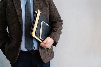 Business professional in a suit holding various folders and notebooks indoors. HD wallpaper