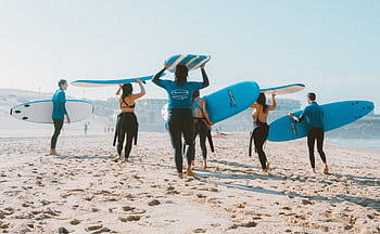 Group of surfers with blue surfboards heading to the ocean on a sunny beach. HD wallpaper