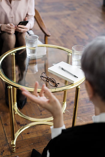 Two adults engaged in a therapy session, seated at a glass table with notebooks and water glasses. HD phone wallpaper