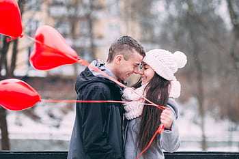 Young couple embracing with red heart balloons outdoors in winter, sharing a joyful moment. HD wallpaper