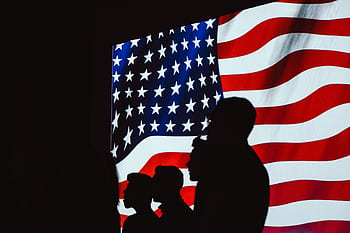 Silhouetted figures in front of a bright, wavy American flag create a patriotic scene. HD wallpaper