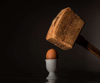 A wooden hammer poised above a fragile egg in a dramatic still life composition. HD wallpaper