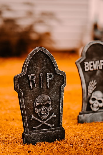 Spooky Halloween tombstones with skull design on vibrant orange grass. HD phone wallpaper