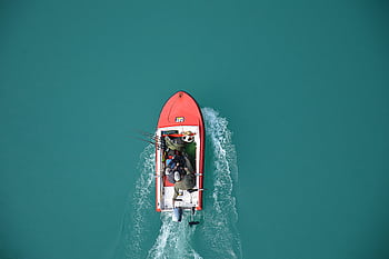 Top view of a red motorboat with fishermen navigating open turquoise waters. HD wallpaper