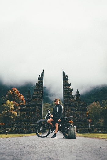 Man posing with motorcycle at iconic Bali temple gate. HD phone wallpaper