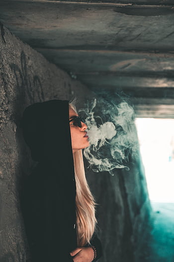Woman in a hoodie exhaling smoke in a moody urban tunnel setting. HD phone wallpaper