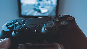 A hand holding a wireless game controller in front of a blurry screen, capturing the gaming experience. HD wallpaper