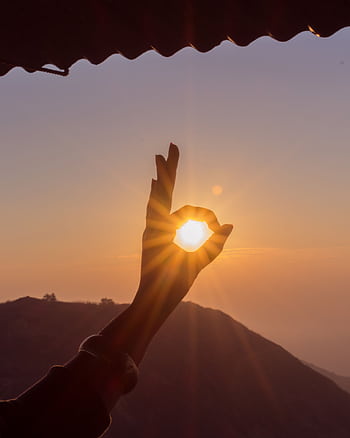 A hand frames the sun at sunset over the Thoptewadi hills, India. HD phone wallpaper