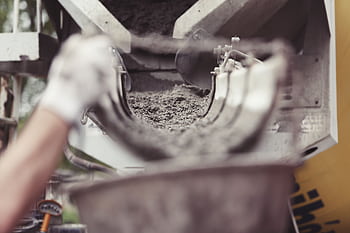Close-up of concrete being poured from a mixer truck at a construction site with a worker's hand visible. HD wallpaper