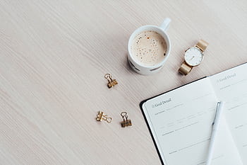 A minimalist desk arrangement featuring a coffee cup, notebook, pen, and wristwatch. HD wallpaper