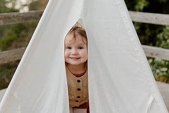 Smiling child peeks out from a cozy tent, exuding joy and playfulness in a natural setting. HD wallpaper