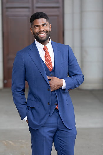 Smiling businessman in a blue suit posing comfortably outdoors with an elegant demeanor. HD phone wallpaper