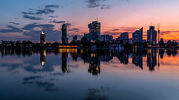 Tranquil reflection of Vienna's cityscape at sunset, showcasing serene waters and vibrant skies. HD wallpaper