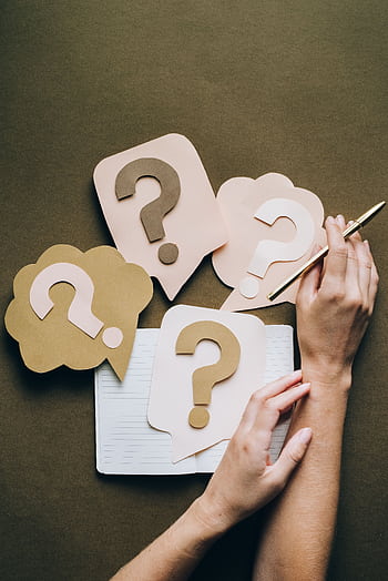 Hands holding pen next to paper question marks on notebook, symbolizing inquiry and creativity. HD phone wallpaper