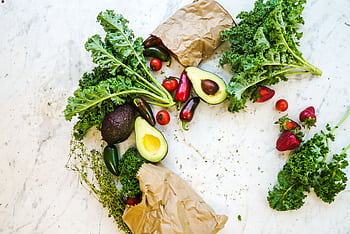 Avocado, kale, and more fresh produce artfully arranged on a marble surface. HD wallpaper
