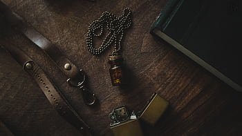 A rustic still life featuring a vintage vial necklace, lighter, and leather strap on a wooden table. HD wallpaper