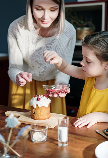 A joyful mother and daughter spend quality time decorating an Easter cake in their cozy kitchen. HD phone wallpaper