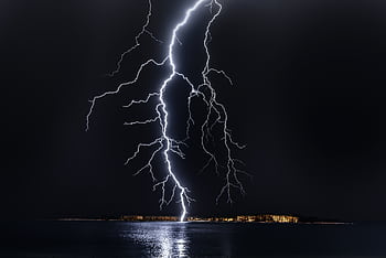 Dramatic lightning bolt over the ocean at night, illuminating the coastal landscape. HD wallpaper