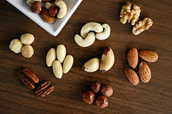 Close-up of various nuts on a wooden table, showcasing healthy snacking options. HD wallpaper