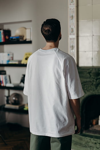 Adult male wearing a white t-shirt stands indoors facing a bookshelf. HD phone wallpaper