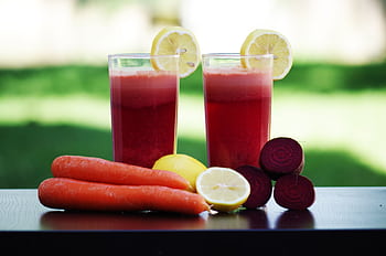 Colorful glasses of beetroot and carrot juice garnished with lemon slices, symbolizing health and freshness. HD wallpaper