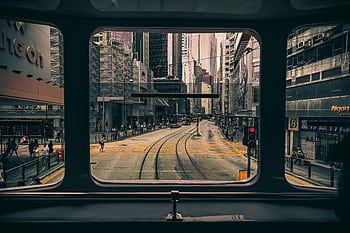 A bustling Hong Kong street seen through a tram window, featuring skyscrapers and public transport. HD wallpaper