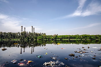 View of a polluted river reflecting factory emissions under a clear sky in India. HD wallpaper