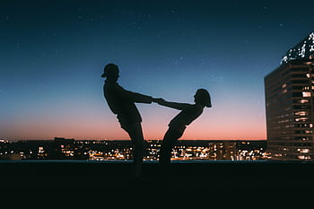 A couple silhouetted against a starry sky on a rooftop in Minneapolis at sunset. HD wallpaper