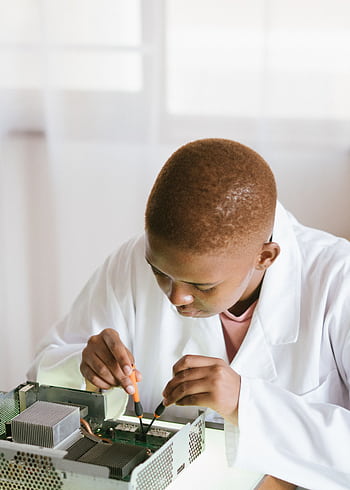 Young technician focusing on electronics repair at a desk indoors. HD phone wallpaper
