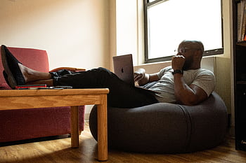 A man working remotely on a laptop while reclining comfortably in a modern home office. HD wallpaper