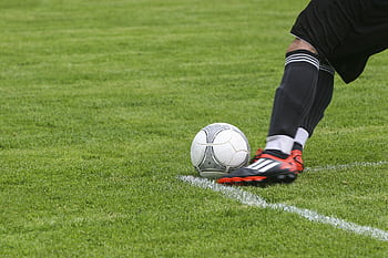 Dynamic shot of a soccer player kicking the ball on a grassy field, showcasing fast-paced sports action. HD wallpaper
