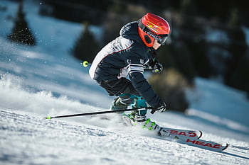 A skier in motion wearing winter gear, gliding swiftly down a snowy slope. HD wallpaper