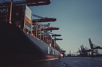 A large cargo ship docked at Hamburg Harbor, cranes loading containers under a clear sky. HD wallpaper