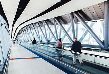 Travelers walking through a bright modern airport corridor with glass walls. HD wallpaper