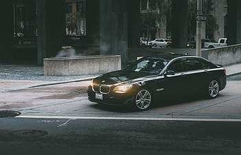 A luxury black car navigating city streets at twilight, showcasing modern city life and design. HD wallpaper