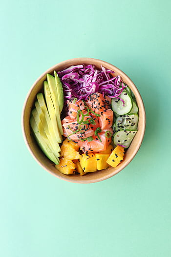 Top view of a vibrant poke bowl with salmon, avocado, mango, and vegetables on a mint background. HD phone wallpaper