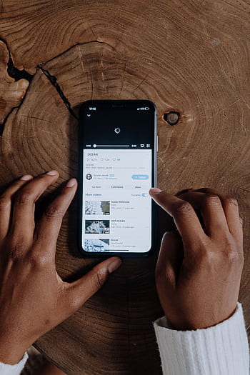 Overhead view of hands browsing videos on a smart placed on a wooden background. HD phone wallpaper