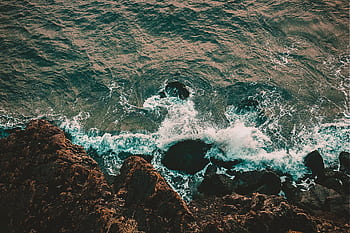 A breathtaking aerial shot of waves crashing on a rocky shoreline, showcasing nature's raw beauty. HD wallpaper