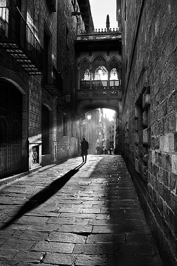A striking black and white scene of a person walking through a historic cobblestone alleyway. HD phone wallpaper