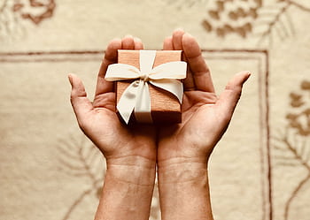 Close-up of hands holding a beautifully wrapped gift box with a ribbon, perfect for celebrations and surprises. HD wallpaper