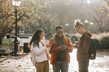 Three diverse young adults enjoying social media together in a sunny park. HD wallpaper