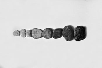 A row of various-sized pebbles arranged on a white surface, capturing texture and form in monochrome. HD wallpaper