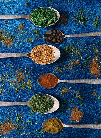 Colorful spices in spoons on a vibrant blue background, showcasing culinary variety. HD phone wallpaper