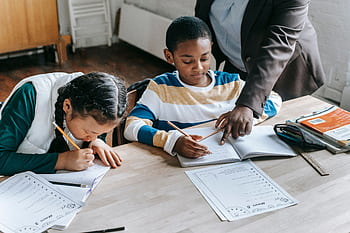 Two children focus on their studies with a teacher's guidance in a classroom setting. HD wallpaper