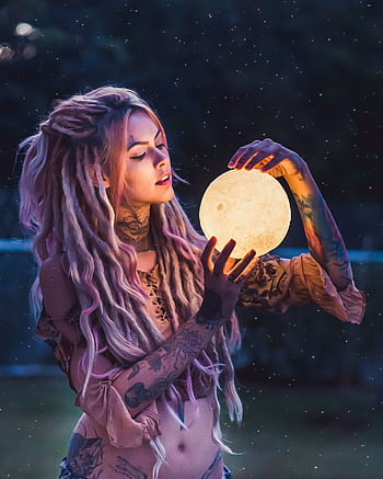 A whimsical outdoor portrait of a tattooed woman holding a glowing orb, conveying mystique and fantasy. HD phone wallpaper