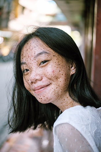 Close-up portrait of a smiling young woman with freckles, capturing a natural and joyful expression outdoors. HD phone wallpaper