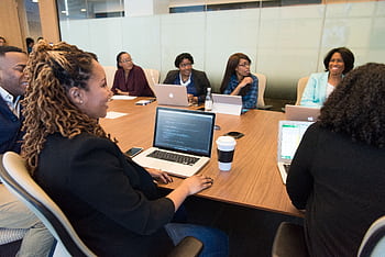 A diverse group of professionals working together in a modern conference room with laptops. HD wallpaper